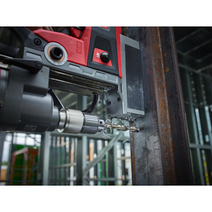 Borrmaskin borrar genom en metallbalk. Kapslade metallspån synliga runt borren.