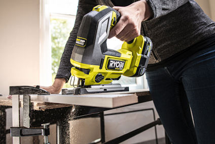 Person använder en grön Ryobi-sticksåg för att såga genom trä.