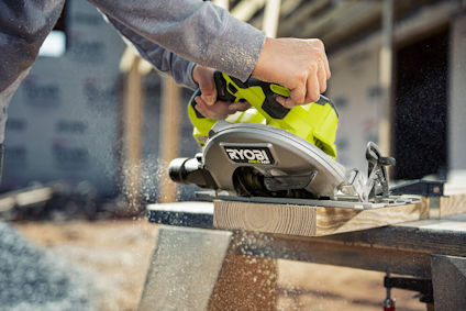 Person använder en grön cirkelsåg med texten "RYOBI" på trästycke.