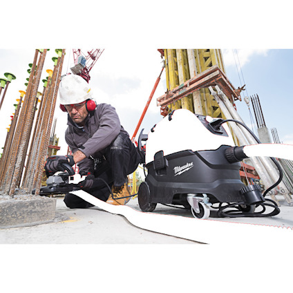 Person i arbetskläder och skyddsutrustning använder en dammsugare vid en byggarbetsplats.