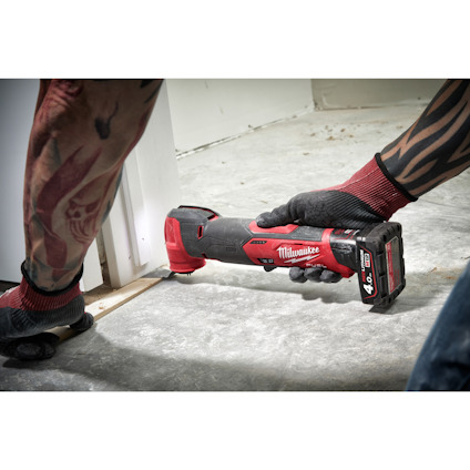 En person använder ett rött Milwaukee multitool för att kapa en sockel nära golvet.