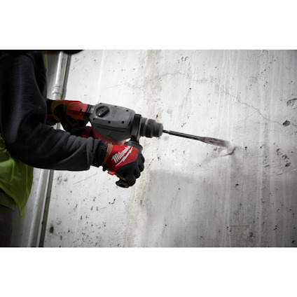 Person som använder en borrhammare mot en betongvägg. Personen bär röda arbetshandskar.