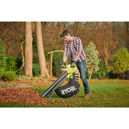 Person rengör löv med Ryobi lövblås/vakuum i trädgård.