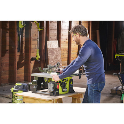 Person med hörselskydd använder en grön och svart sågmaskin i ett träverkstad.