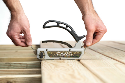 Person använder verktyg för att installera trall på träbjälkar. Verktyget är märkt "CAMO".