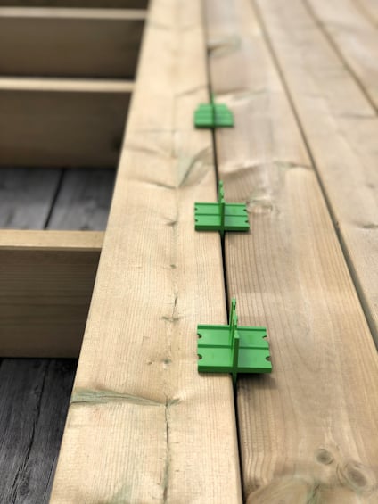 Trallbrädor med gröna distansverktyg mellan dem, används vid konstruktion av trädäck.