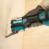 Hand håller en Makita multiverktyg mot träyta med en markering. Verktyget har etiketten "Starlock Max".