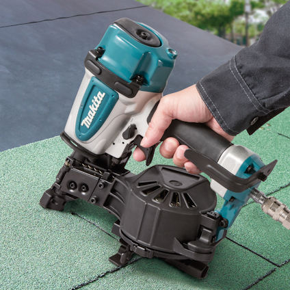 Hand använder en tryckluftdriven spikpistol på grön yta med Makita-logotyp.