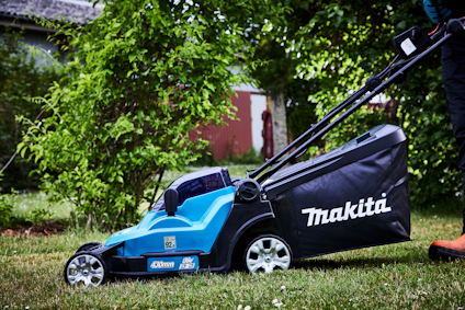 Gräsklippare med blå och svart design, märkt "Makita", används på en gräsmatta bredvid gröna buskar.