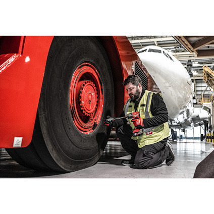 Person i gul väst arbetar på stort flygplanshjul i hangar.
