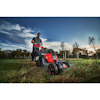 Man in sunglasses pushing a red and gray lawnmower on a grassy field under a blue sky with clouds.