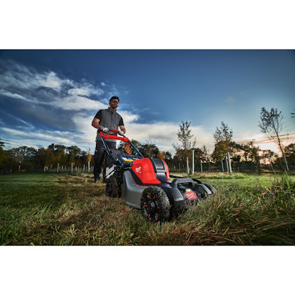Man in sunglasses pushing a red and gray lawnmower on a grassy field under a blue sky with clouds.