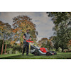 Man pushing a lawnmower on grass, surrounded by trees with autumn foliage.