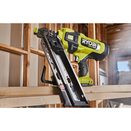 Spikpistol från Ryobi placerad på en träbjälke i en byggmiljö.