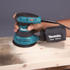 En hand håller en Makita excenterslip på en träyta.