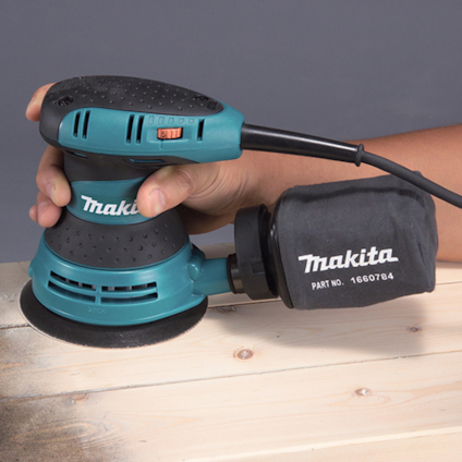Person använder en blå och svart Makita slipmaskin på träyta.