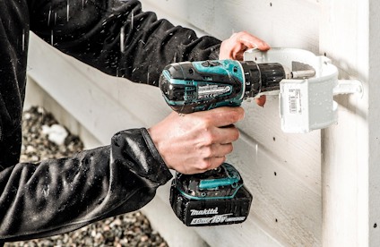 En person skruvar fast en rännkrok på vit träfasad.