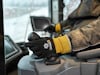En person i arbete bär handskar och styr en maskin med en joystick i en förarhytt.
