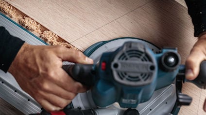 Händer håller en cirkelsåg och skär en träplanka.