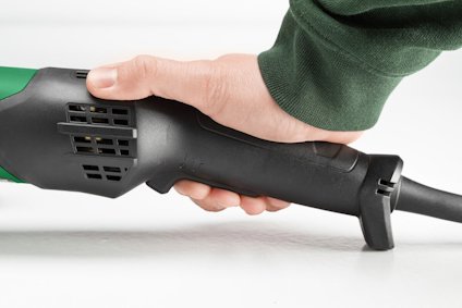 Hand som håller i ett elverktygs handtag i svart och grönt, med synlig sladd.