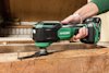 Person använder en grön och svart HiKOKI multiverktyg för att skära trä nära en spik.