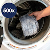 Hand placerar en grå, lurvig trasa i en tvättmaskin. Texten "500x" syns på en blå cirkel i bilden.