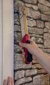 Häftpistol med rött handtag används mot en vägg med stenliknande tapet.
