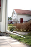 Vit stuprör vid ett hus, leder regnvatten bort över en plattlagd gång. Hus med rött tak syns i bakgrunden.