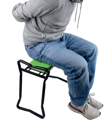 Person sitter bakåtvänd på en grön stol med svart metallram, händerna bakom ryggen, grå huvtröja, blå jeans och grå skor.